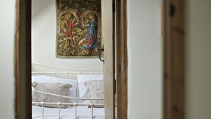 A narrow hallway leading to a bedroom with a bed, a radiator, and a tapestry on the wall.
