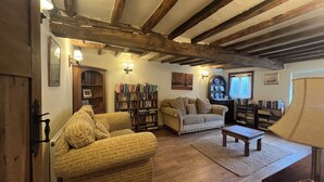 A cozy living room with exposed wooden beams, a sofa, a coffee table, and a bookshelf filled with books.