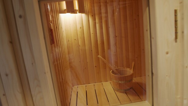 A wooden sauna with a window, a wooden bucket, and a wooden bench.