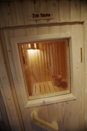 A wooden sauna with a window, a wooden bucket, and a wooden bench. - White Horse Cottage  with Sauna (Wellow)