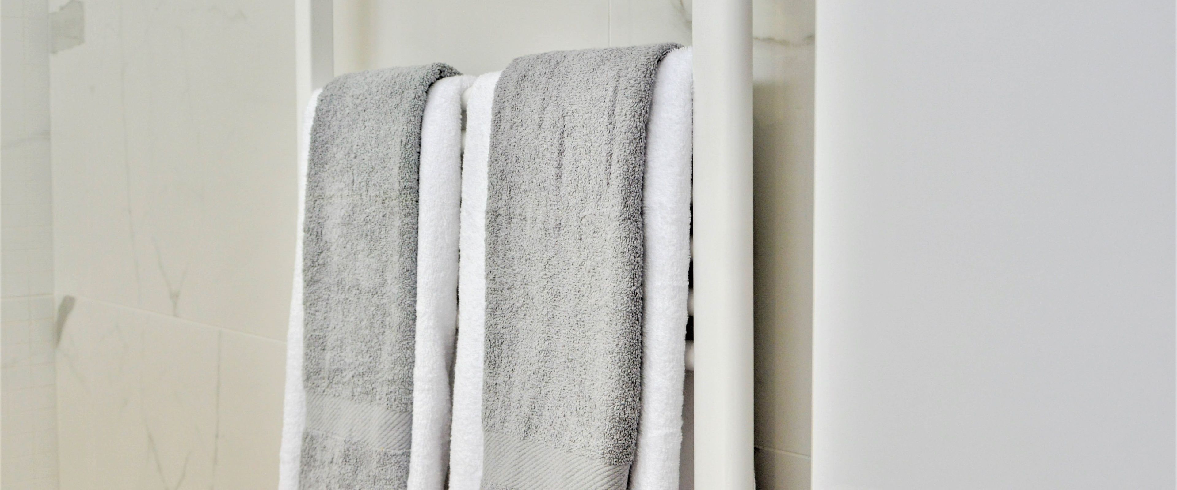 A bathroom with a white tiled wall and two towels hanging on a towel rack.