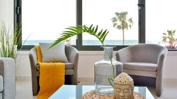En moderne stue med havudsigt, med to grå lænestole, en glasvase med en plante og en Buddha-statue på en vævet bakke.