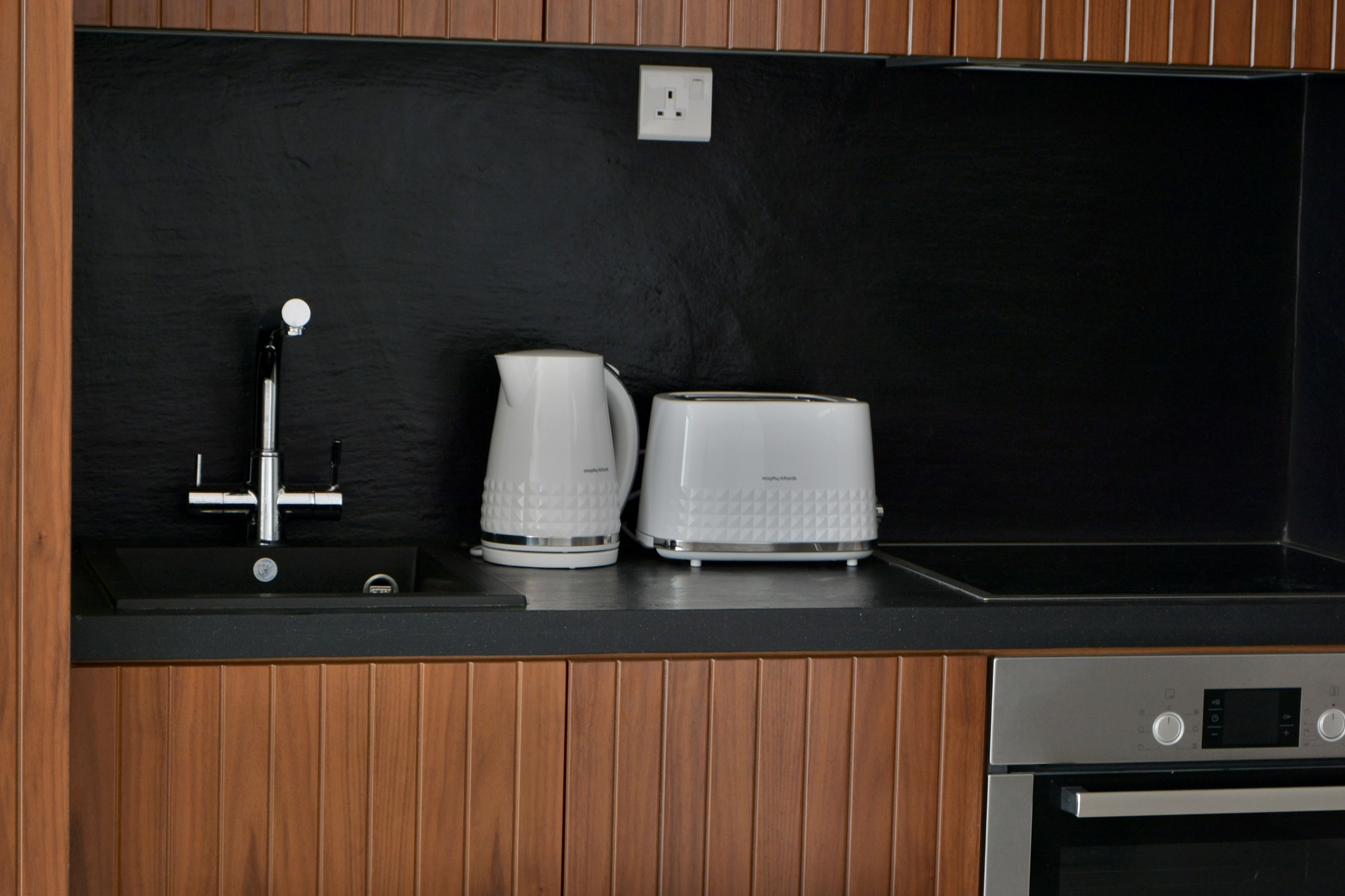 A kitchen with a black countertop, a coffee maker, a toaster, and a stainless steel oven.