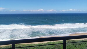 A view of the ocean with waves crashing onto a sandy beach, viewed from a balcony with a railing. - 504 Coral Reef (La Mercy)