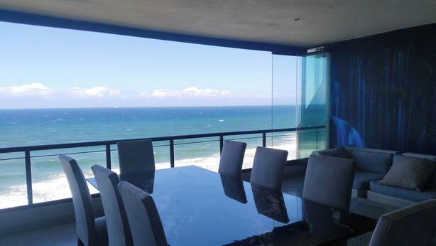 A modern balcony with a glass railing overlooking the ocean. There is a dining table with chairs and a sofa with cushions. - 504 Coral Reef (La Mercy)