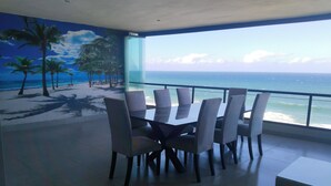 A dining area with a view of the ocean, featuring a table and chairs, and a mural of a beach scene. - 504 Coral Reef (La Mercy)
