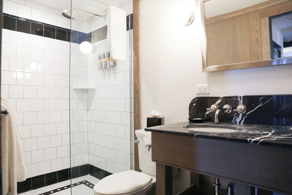 Ein Badezimmer mit Duschkabine aus Glas, einer weißen Toilette und einem dunklen Marmorwaschbecken.