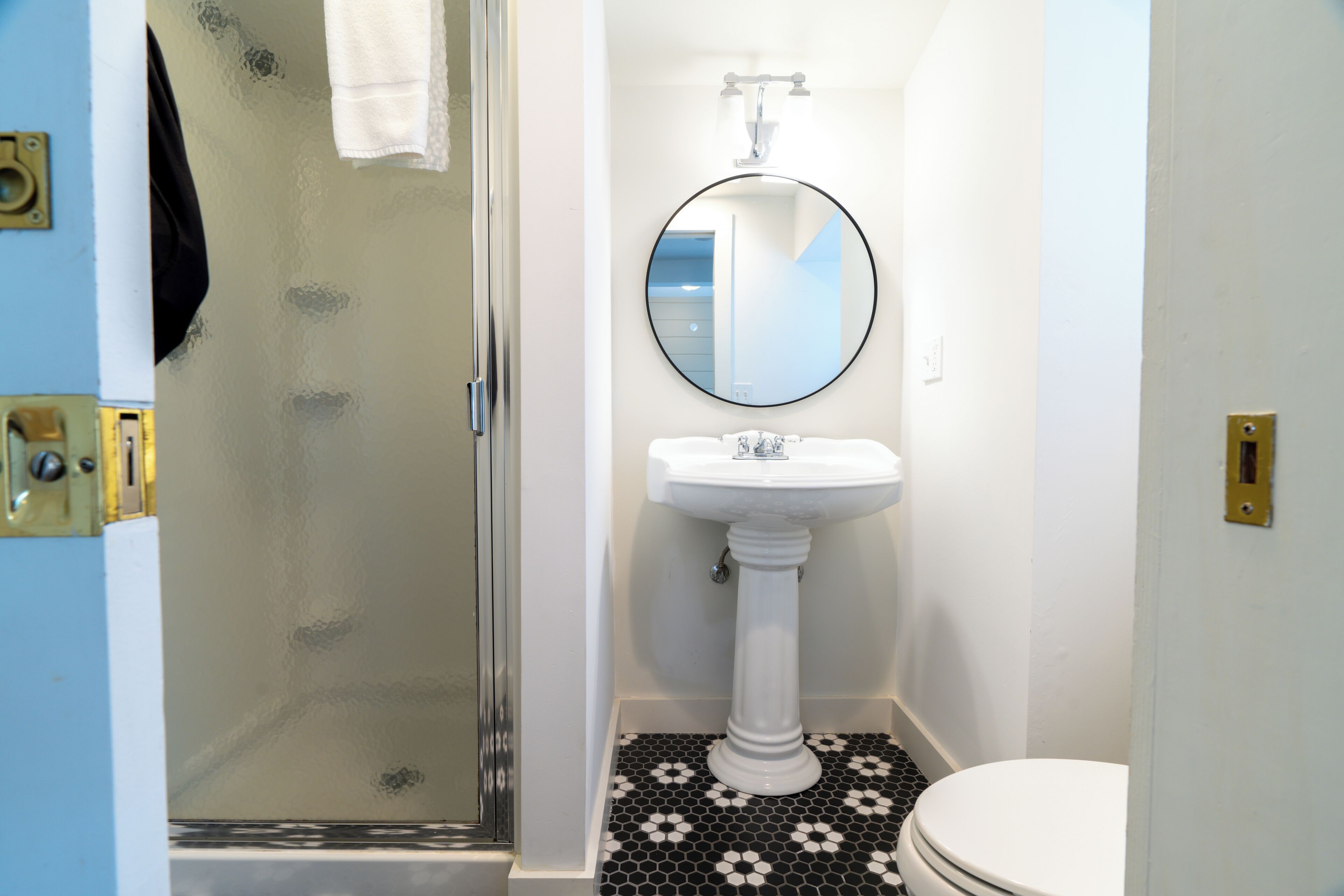 Un baño con un lavamanos pedestal blanco, un espejo redondo y un inodoro.