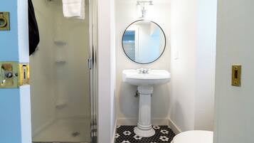 Un baño con un lavamanos pedestal blanco, un espejo redondo y un inodoro.
