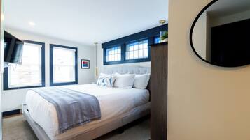 A neatly arranged bedroom with a large bed, a wooden headboard, a mirror, and a window with blinds.