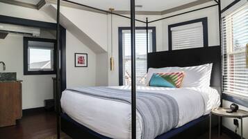 A four-poster bed with a white and blue bedspread, a small bedside table with a lamp, and a window with blinds.