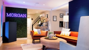 A modern living room with a sofa, armchairs, and a coffee table. A neon sign with the name "MORGAN" is visible on the wall. - Morgan Hotel (Oak Bluffs)