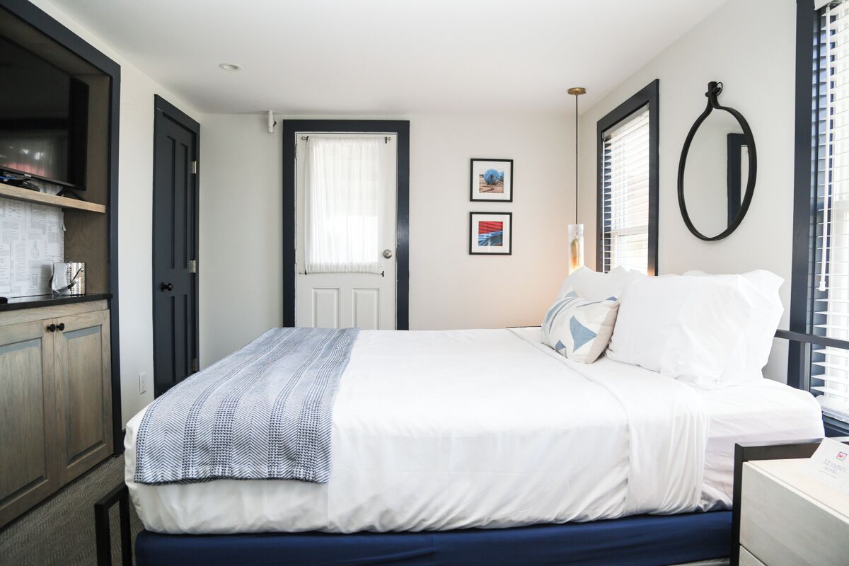 A neatly arranged bedroom with a bed, a bedside table, a wardrobe, and a door leading to another room.