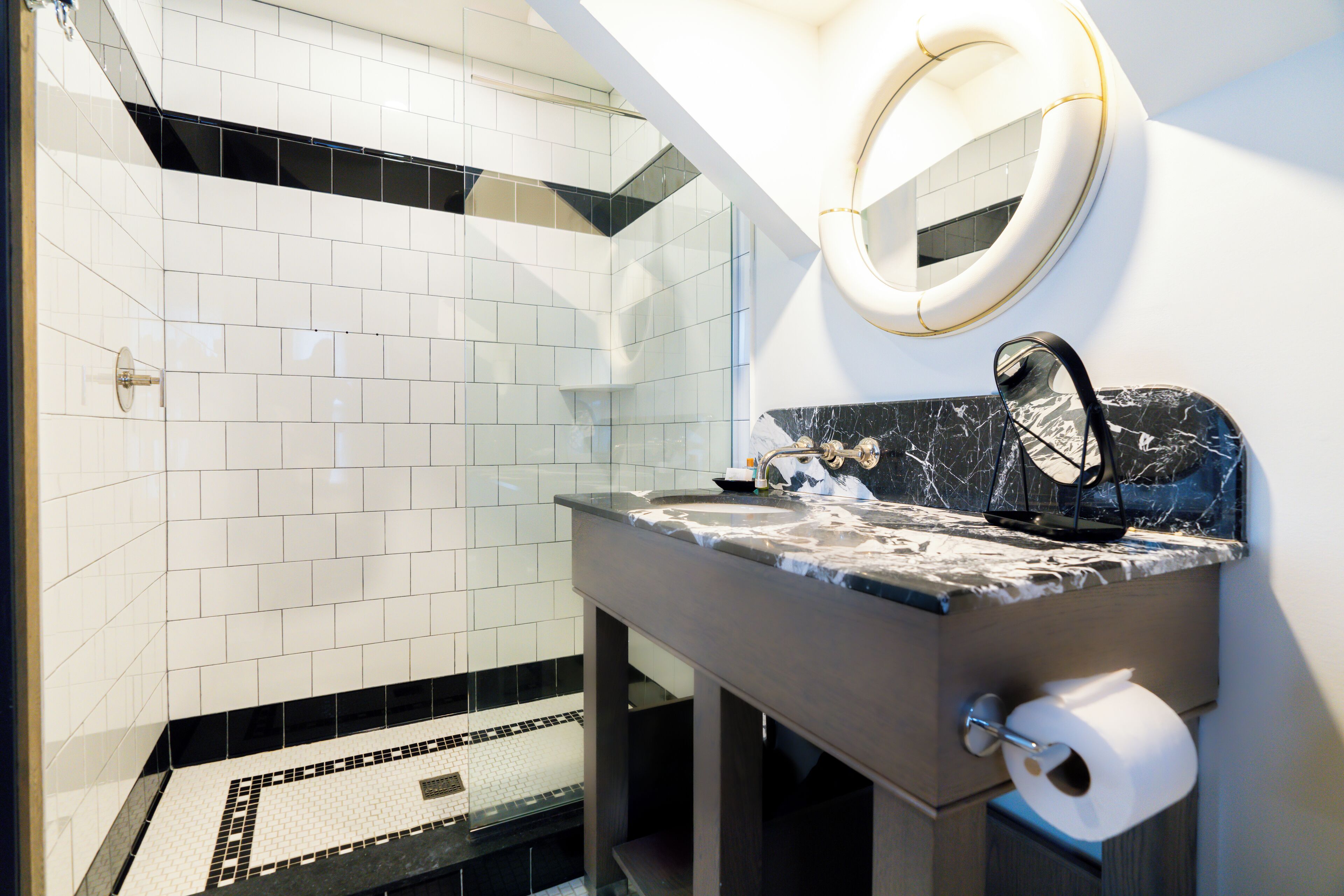 A modern bathroom with white tiles, a marble countertop, a sink, a mirror, and a toilet paper holder.