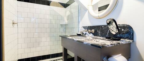 A modern bathroom with white tiles, a marble countertop, a sink, a mirror, and a toilet paper holder.