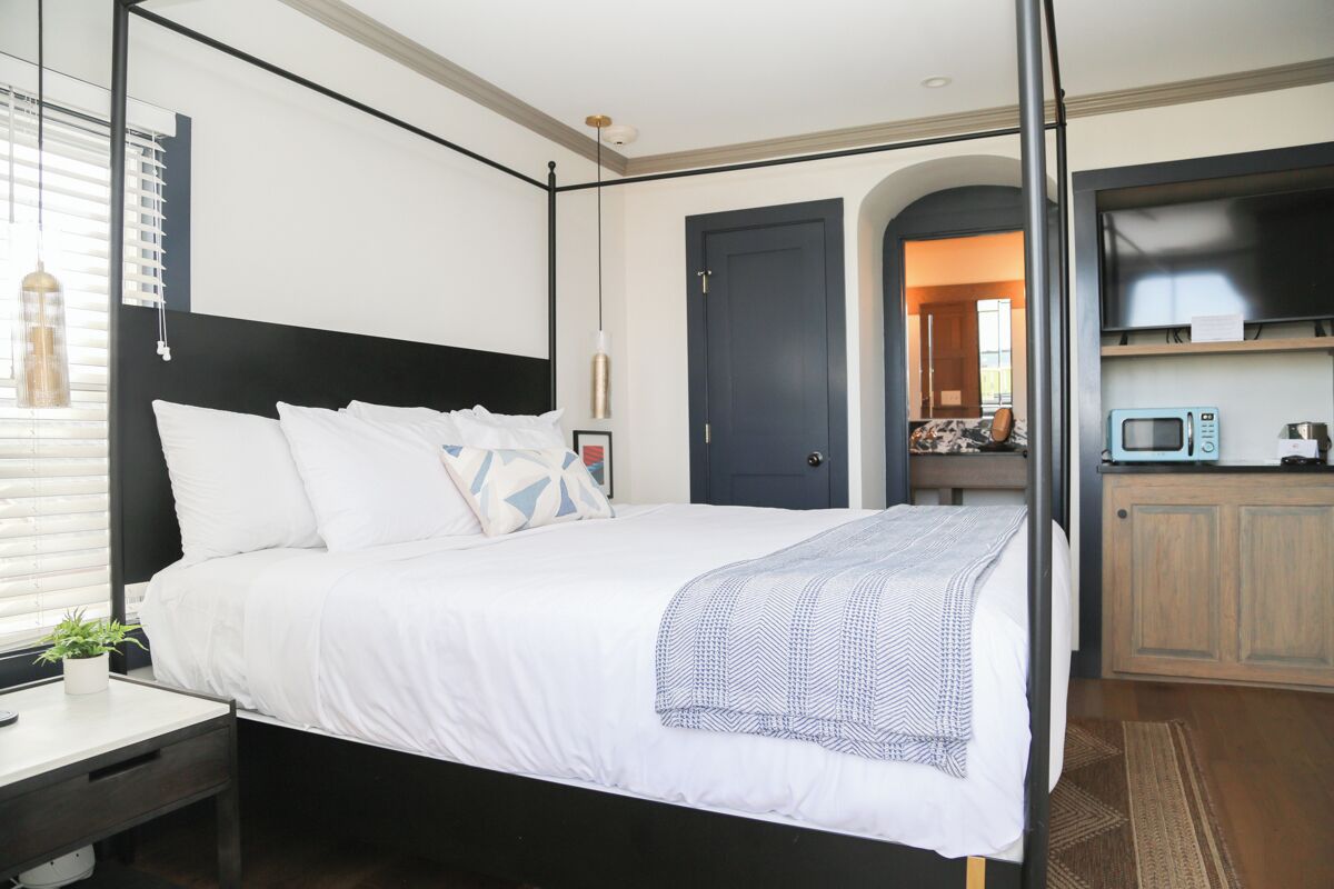 A modern bedroom with a large bed, bedside tables, a TV, and a kitchenette area.