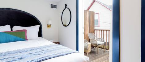 Ein Schlafzimmer mit Bett, Spiegel und Blick auf eine Terrasse mit Stühlen.