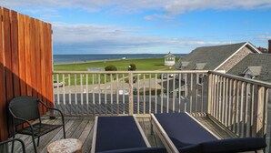 A balcony with two lounge chairs, a small round table, and a view of the beach and ocean. - Morgan Hotel (Oak Bluffs)
