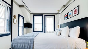 A bedroom with a bed, a TV, and a window with blinds. - Morgan Hotel (Oak Bluffs)