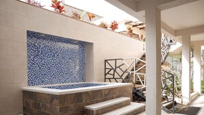 Een wellnessruimte met een betegelde muur, een whirlpool en een trap naar een hoger niveau.