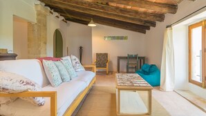 A cozy living room with a wooden ceiling, a sofa with patterned cushions, a small table, and a teal bean bag. - SON BANUS - Chalet with private garden in Manacor. Free WiFi (Manacor)
