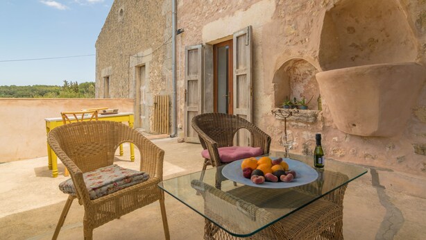 A rustic stone building with a glass table and wicker chairs, a plate of fruit, and a bottle of wine. - SON BANUS - Chalet with private garden in Manacor. Free WiFi (Manacor)