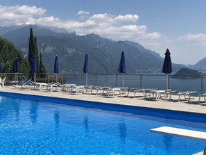 A swimming pool with lounge chairs and umbrellas, overlooking a lake with mountains in the background. - Terraces-Luxury Lake Como View Apartment in Menaggio  (Menaggio)