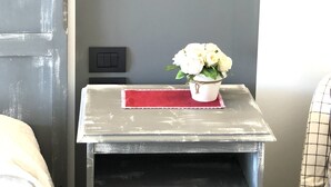 Een kamer met een grijze muur, een klein tafeltje met een rode placemat en een vaas witte bloemen.
