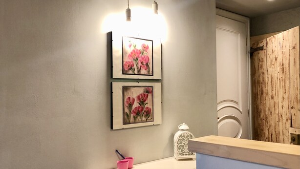 Et badeværelse med et hvidt toiletbord, to billeder af blomster i rammer, en hvid lanterne og et spejl med en træpanel.