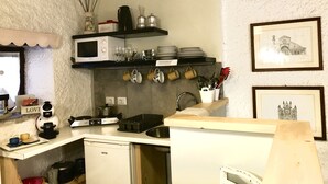 Et lille køkken med ovn, komfur og vask. Hylder med service og bestik, samt et lille køleskab.