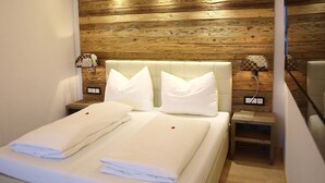 A neatly made bed with white linens in a modern room with wooden paneling on the walls and a small bedside table with a lamp. - Luxury Apartment Schoenbichl (Sankt Johann in Tirol)