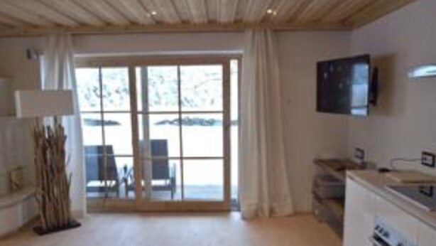 A modern kitchen with a large window, a flat-screen TV, and a dining area with a table and chairs. - Luxury Apartment Schoenbichl (Sankt Johann in Tirol)