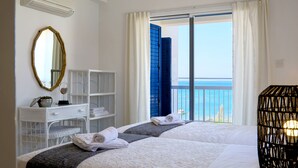 A hotel room with two beds, a white dresser, a mirror, and a balcony with blue shutters.