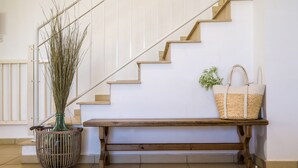 A staircase with a wooden bench at the bottom, a woven basket on the wall, and a tall plant in a striped pot.
