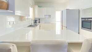 A modern kitchen with white cabinetry, a central island, a built-in oven, and a refrigerator.