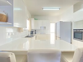 Una cocina moderna con armarios blancos, una isla central, horno empotrado y refrigerador.