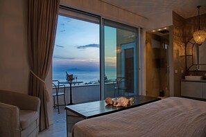 Habitación de hotel moderna con un gran ventanal corredero que da a un balcón con vistas al mar. La habitación tiene una cama, un escritorio y una silla.