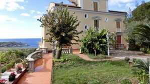 A two-story building with a balcony, surrounded by greenery and a clear view of the sea. - Villa Rufola (Sorrento)