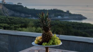 A fruit platter on a table with a scenic coastal view in the background. - Villa Rufola (Sorrento)