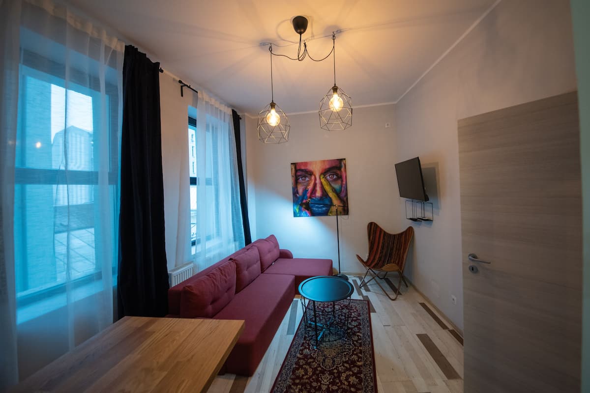 Un salon moderne avec un canapé rouge, une table basse en bois et un tapis à motifs. On y trouve deux luminaires suspendus et un tableau accroché au mur.
