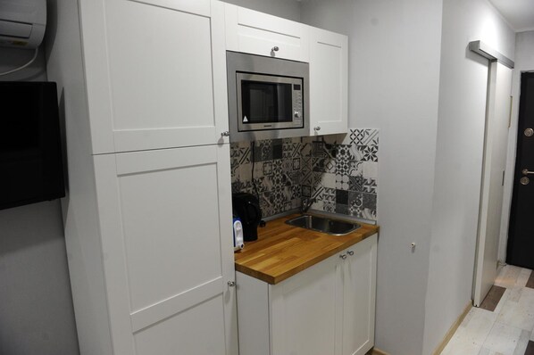 A compact kitchen with white cabinets, a microwave, a sink, and patterned backsplash tiles.