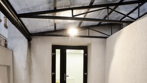 En overdækket trappe fører op til en dør med glasrude, metal tag og betondæk.