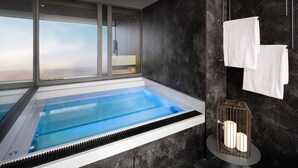 A modern bathroom with a large bathtub, a window with a view, and a round table with candles. - Wellness- & Sporthotel Jagdhof (Roehrnbach)