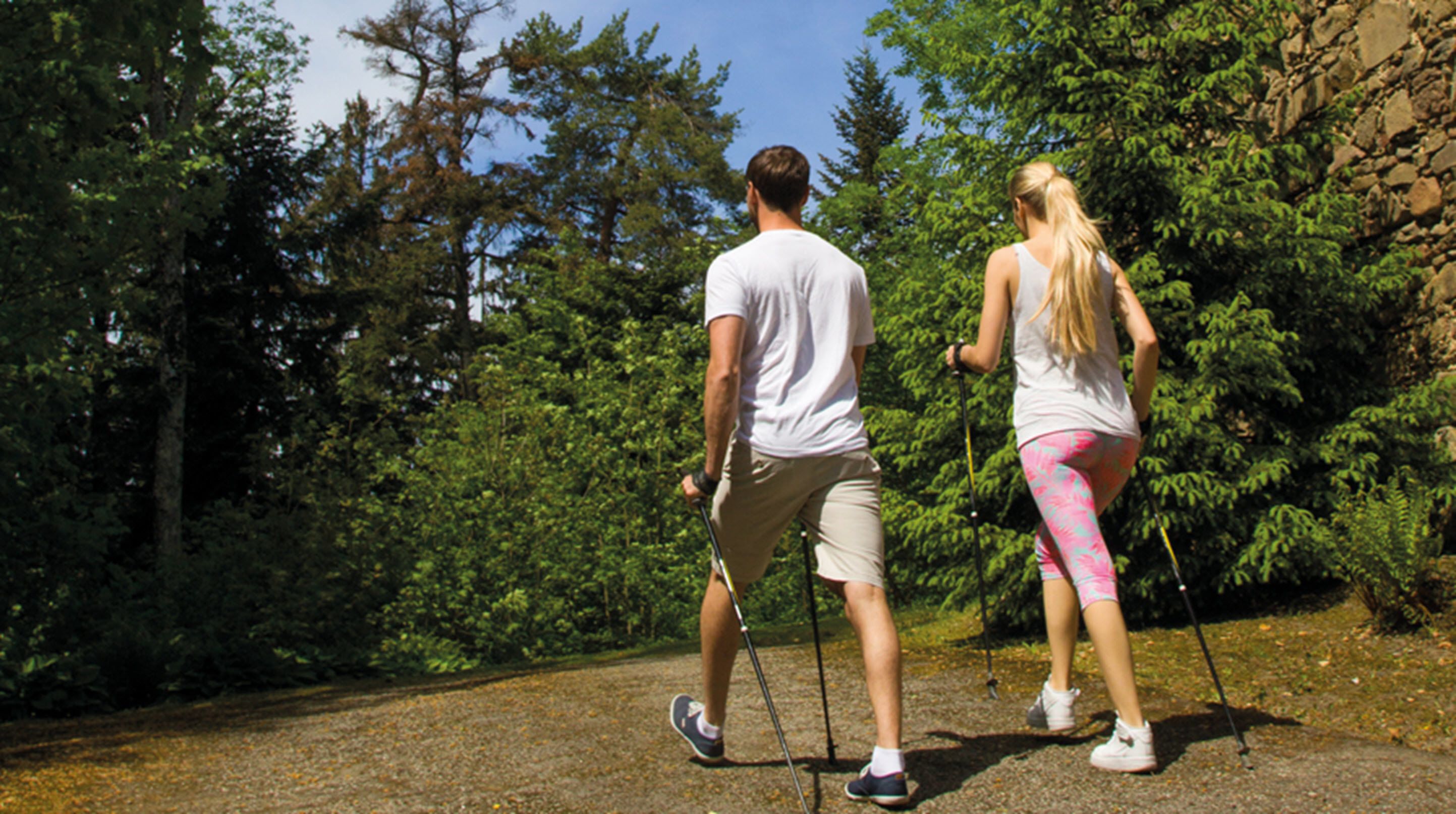 A couple hiking on a gravel path surrounded by dense green foliage and trees.