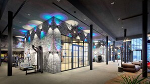 A modern gym with exercise equipment, a glass door entrance, and a ceiling with colorful lighting. - Wellness- & Sporthotel Jagdhof (Roehrnbach)