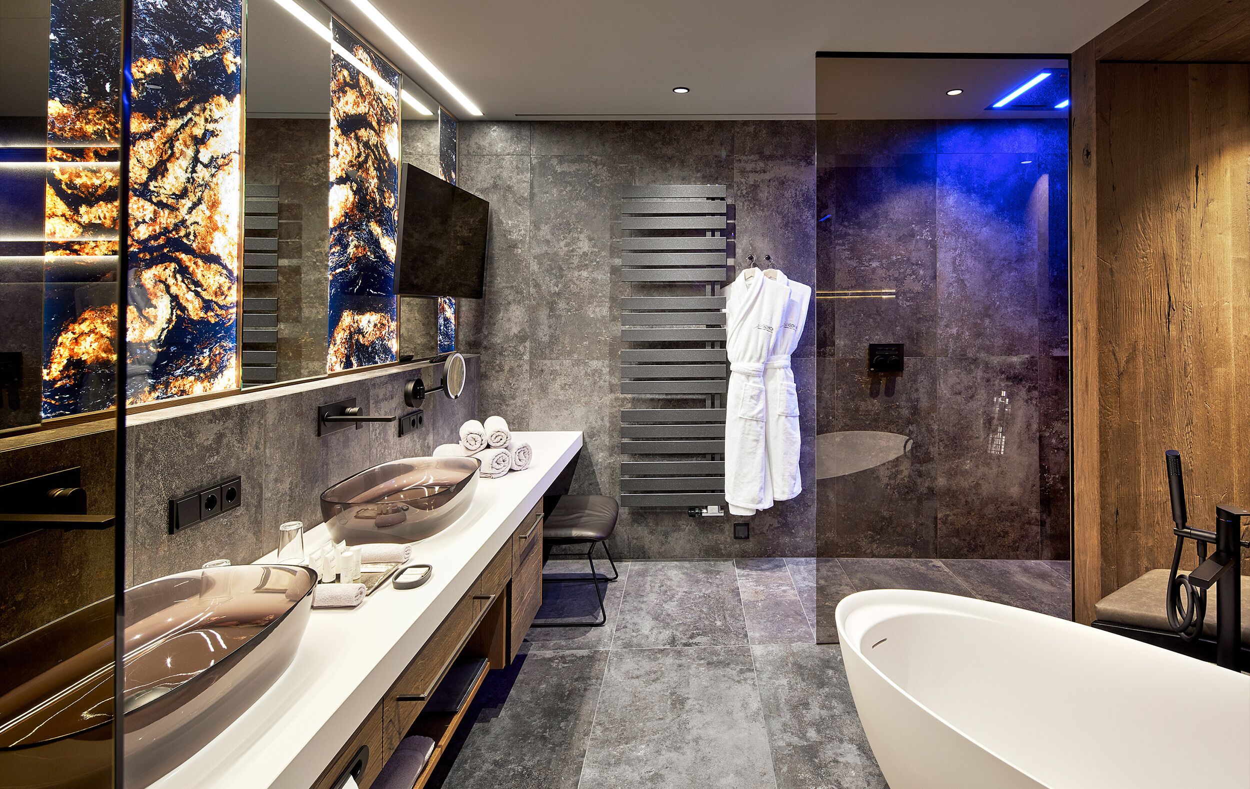 A modern bathroom with a large mirror, two sinks, a bathtub, and a towel rack.