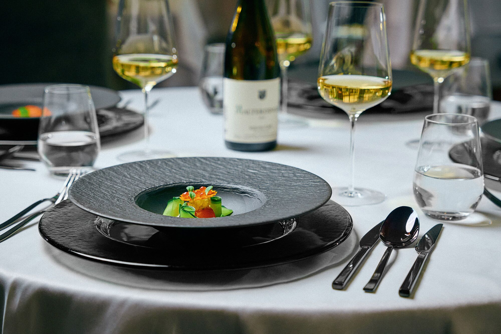 Una elegante disposición para comedor con un plato negro, mantel blanco y cristalería transparente.