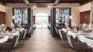 A restaurant with multiple tables, each set with white tablecloths and grey chairs. There are shelves with bottles and glasses on the walls. - Wellness- & Sporthotel Jagdhof (Roehrnbach)