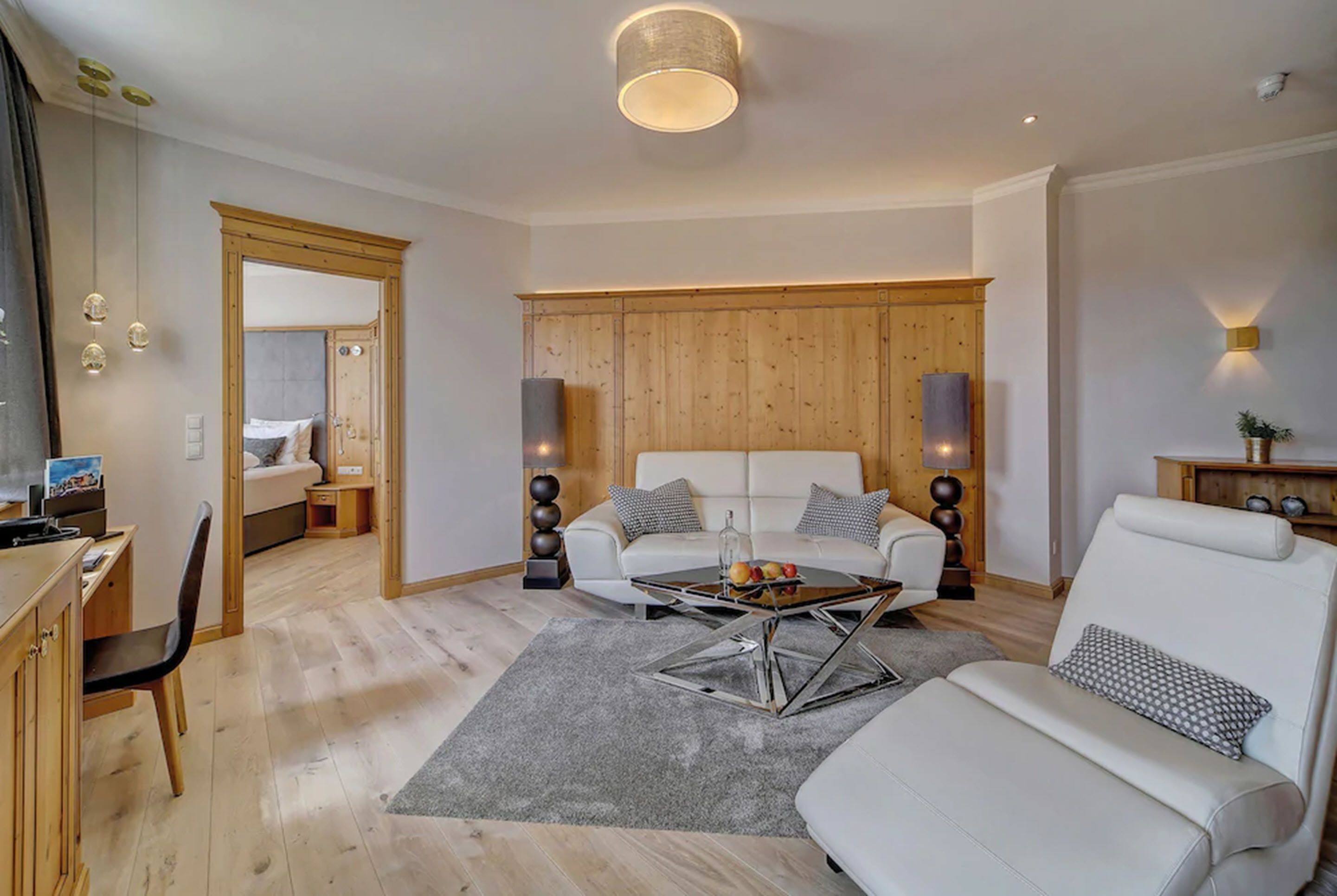 Una sala moderna con un sofá, una mesa de centro y un televisor. Se observa un mueble de madera y un escritorio con una silla.