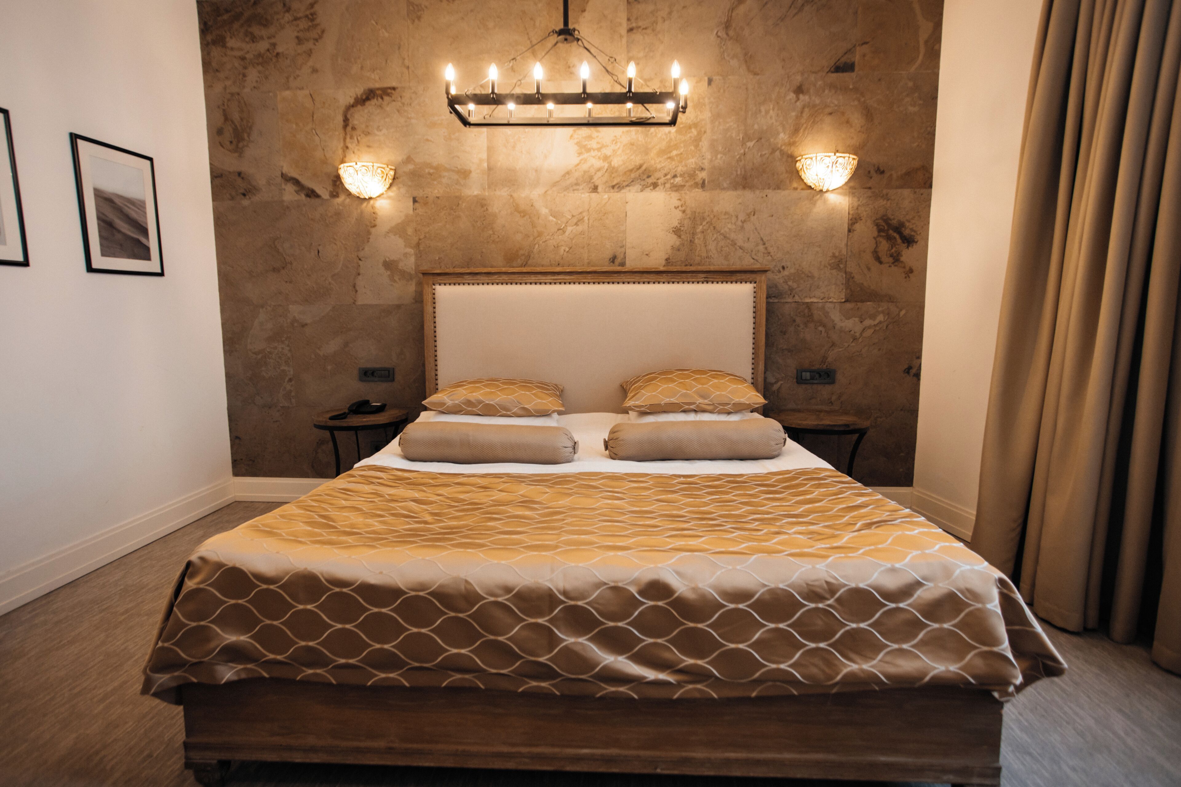 A bedroom with a large bed, two bedside tables, a chandelier, and a stone wall.